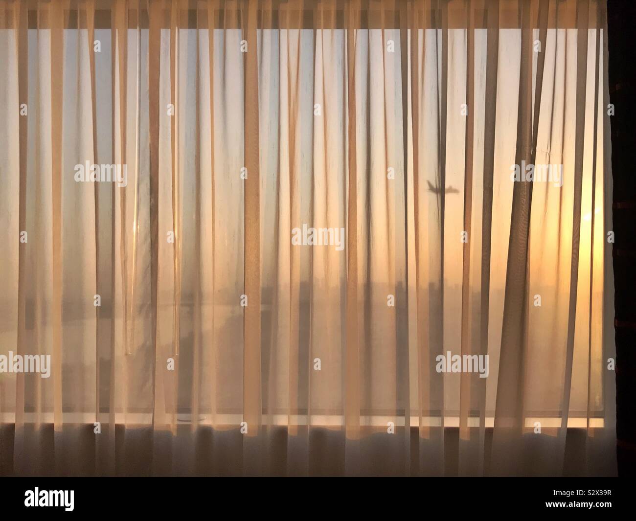 Hotel curtained window: view of sunrise with an aéroplane passing by - Smartphone Captured Stock Image