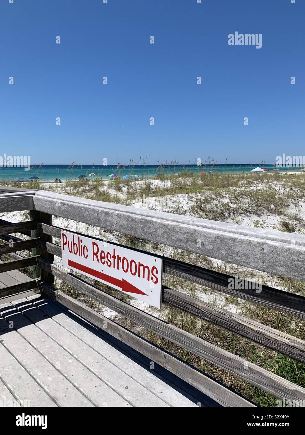 Public restroom sign on the beach with view of sand dunes and water