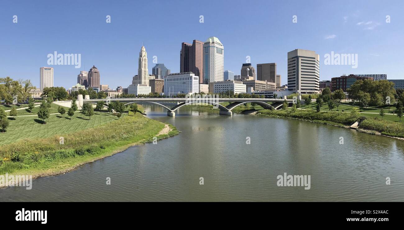 The Columbus, Ohio downtown cityscape is shown in a panoramic view, with the Scioto River and Discovery Bridge in the foreground. - Smartphone Captured Stock Image