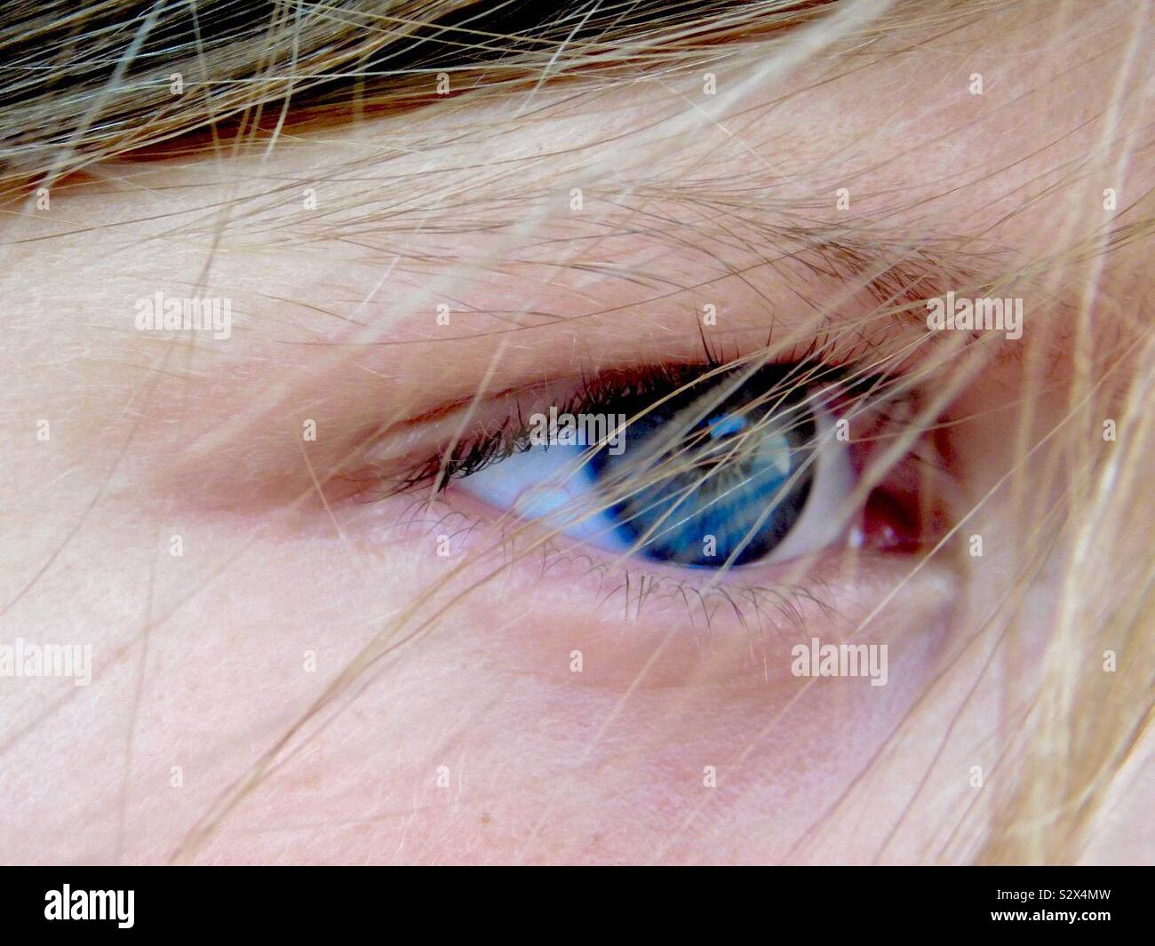 Sideways perspective of child’s blue eyes with wind blowing hair in way. Stock Photo