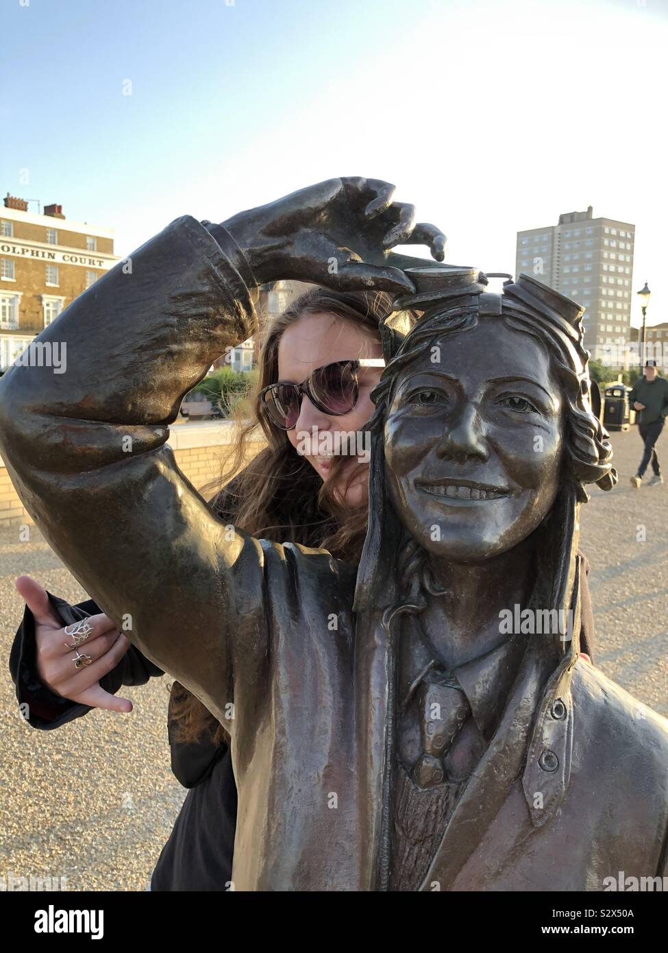 A young woman (and Amy Johnson look a like) poses joyfully with the Amy Johnson aviation sculpture at Herne Bay, Kent and captures the mood of the statue. Stock Photo