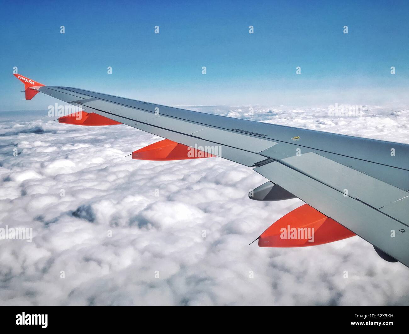 The view out of an EasyJet aircraft window whilst at cruising altitude. Above the clouds & below a blue sky - holidays beckon! Photo Credit - © COLIN HOSKINS. - Smartphone Captured Stock Image