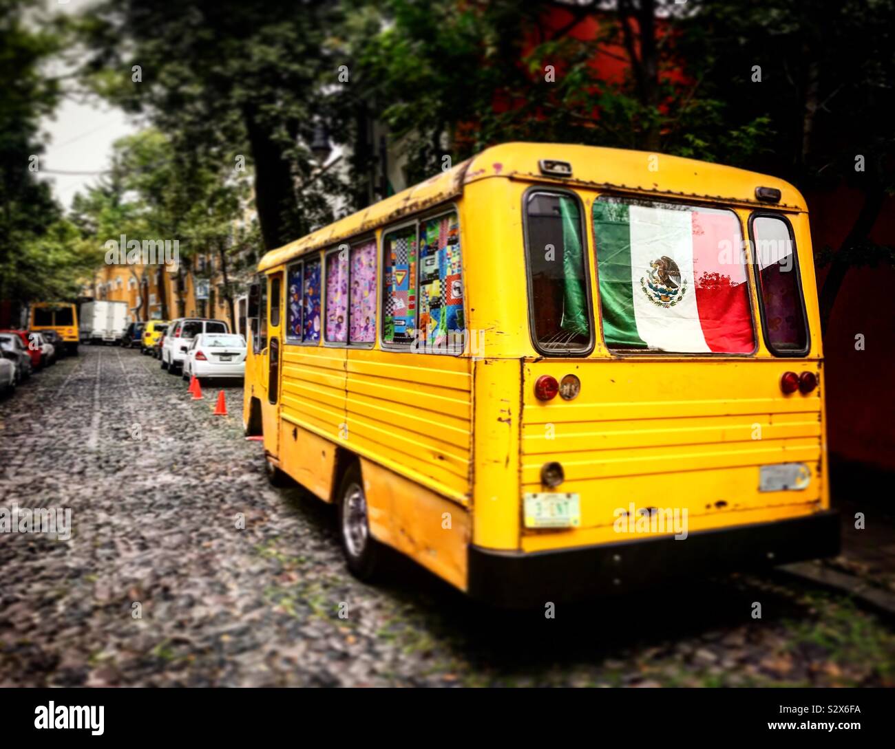 A yellow bus decorated with the Mexican flag in a street of San Angel, Mexico City, Mexico Stock Photo