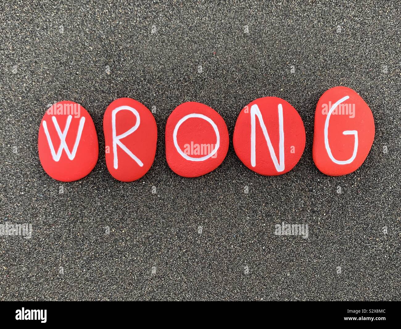 Wrong text composed with carved and red colored stones over black volcanic sand - Smartphone Captured Stock Image