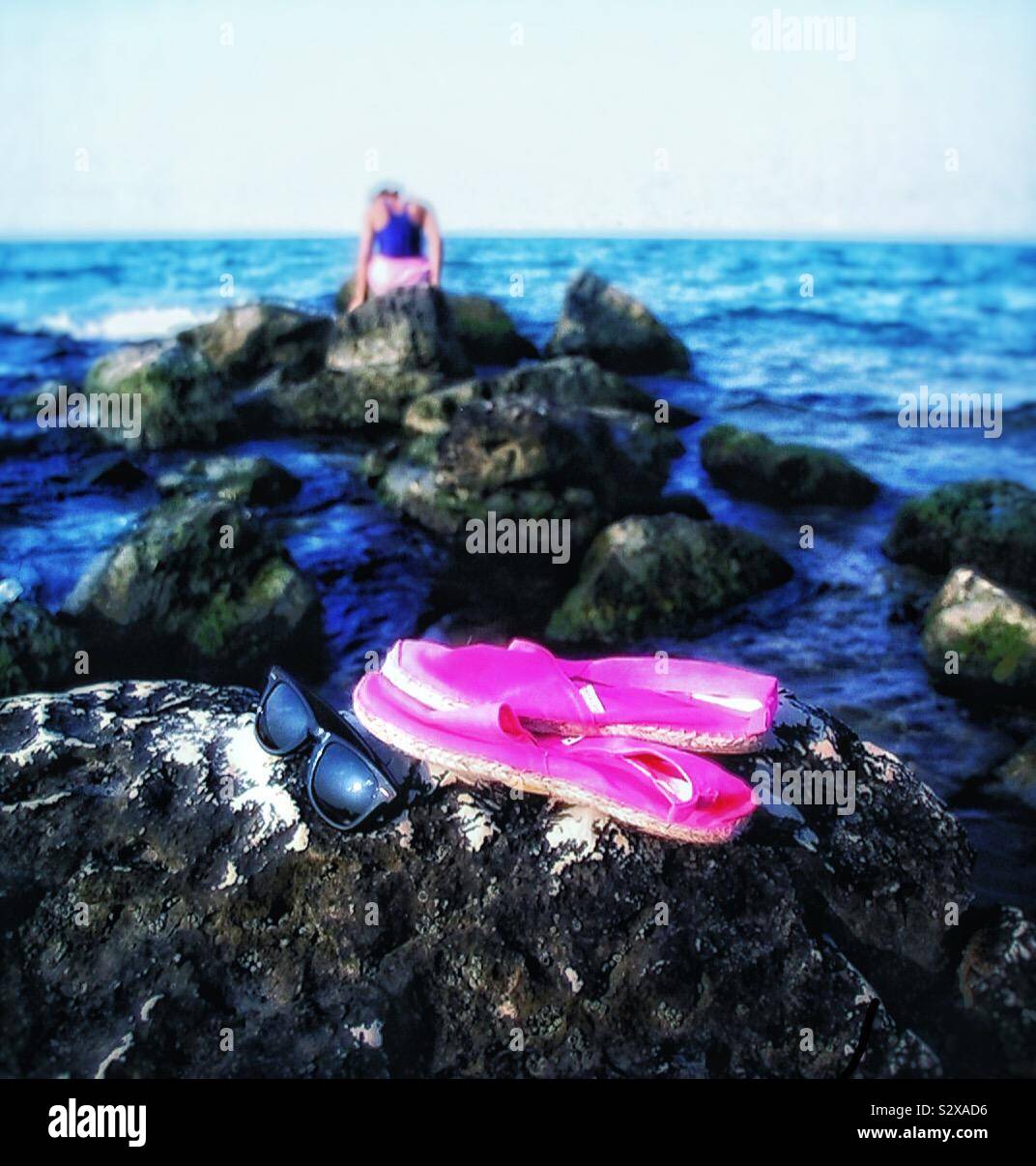 A young woman sits on the rocky beach. - Smartphone Captured Stock Image