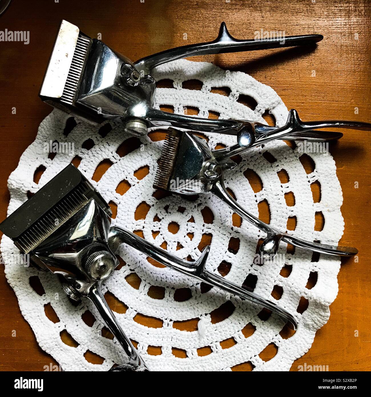 A collection of 3 three hand-operated manual hair clippers gathered together on a doyley on top of a table top Stock Photo