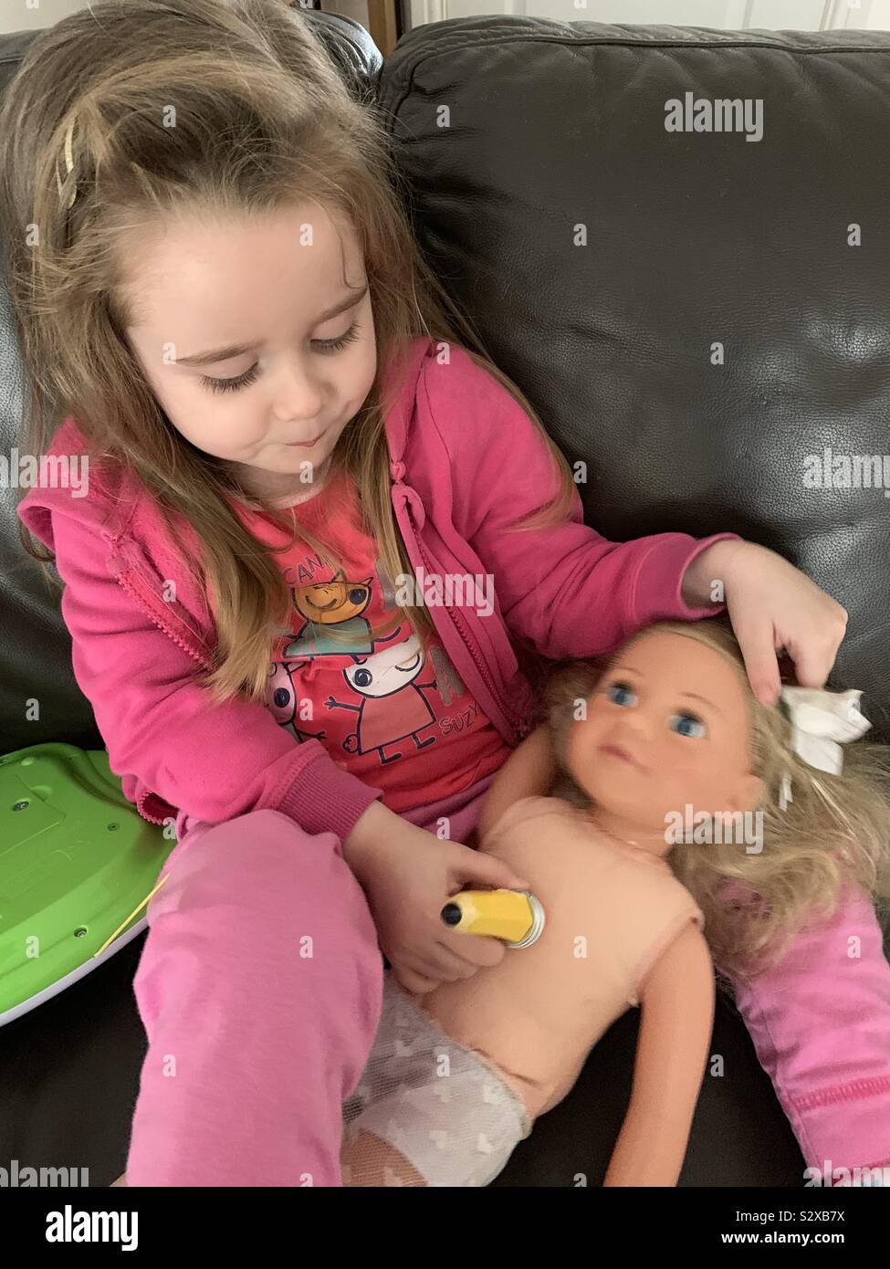 Little girl pretending to be examining her poorly doll Stock Photo