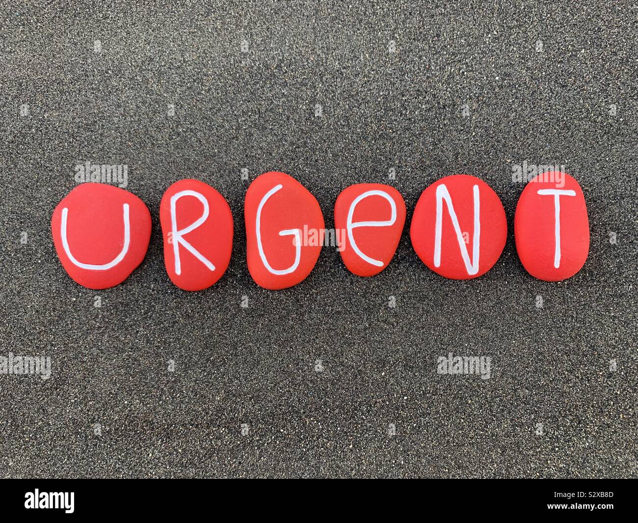 Urgent text composed with red colored stones over black volcanic sand - Smartphone Captured Stock Image