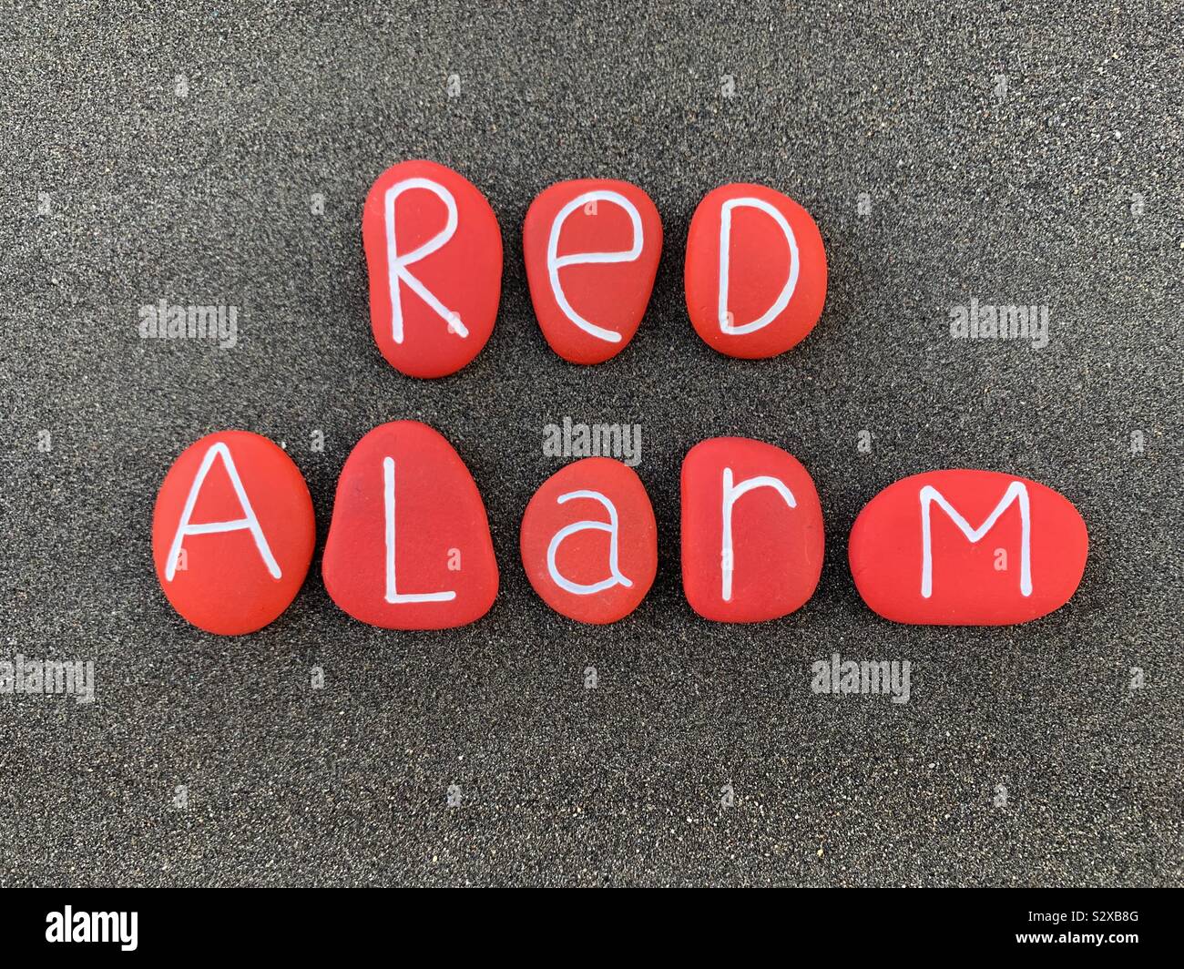 Red Alarm text composed with red colored stones over black volcanic sand - Smartphone Captured Stock Image