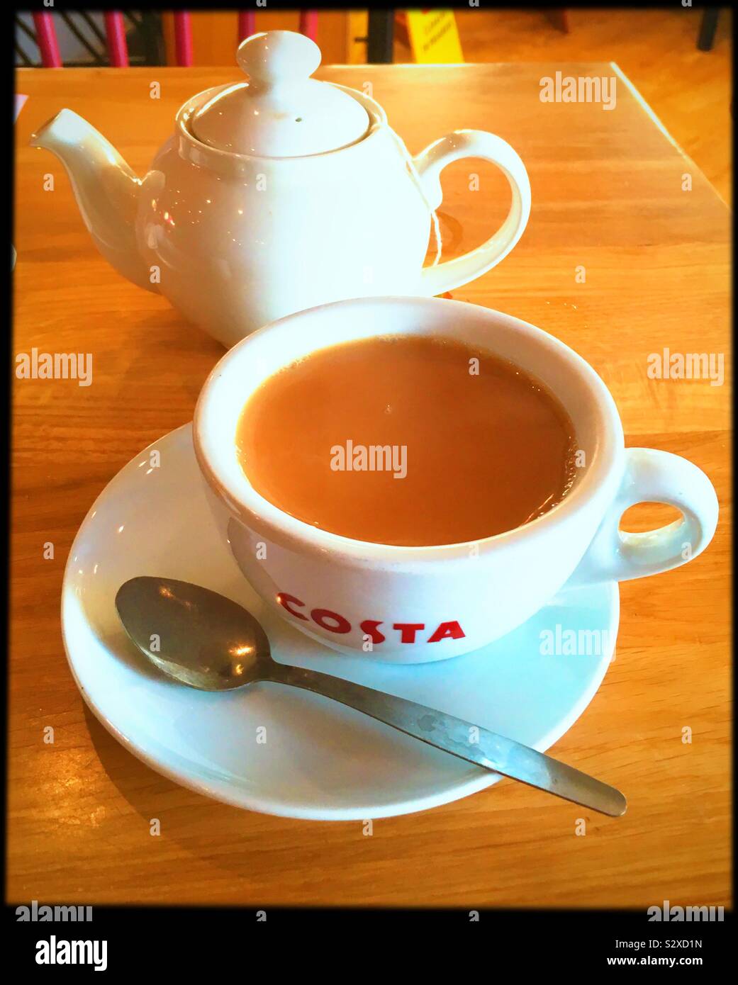 A cup of tea in a cafe with white cup and saucer, white teapot and a teaspoon, on a wooden table. Stock Photo