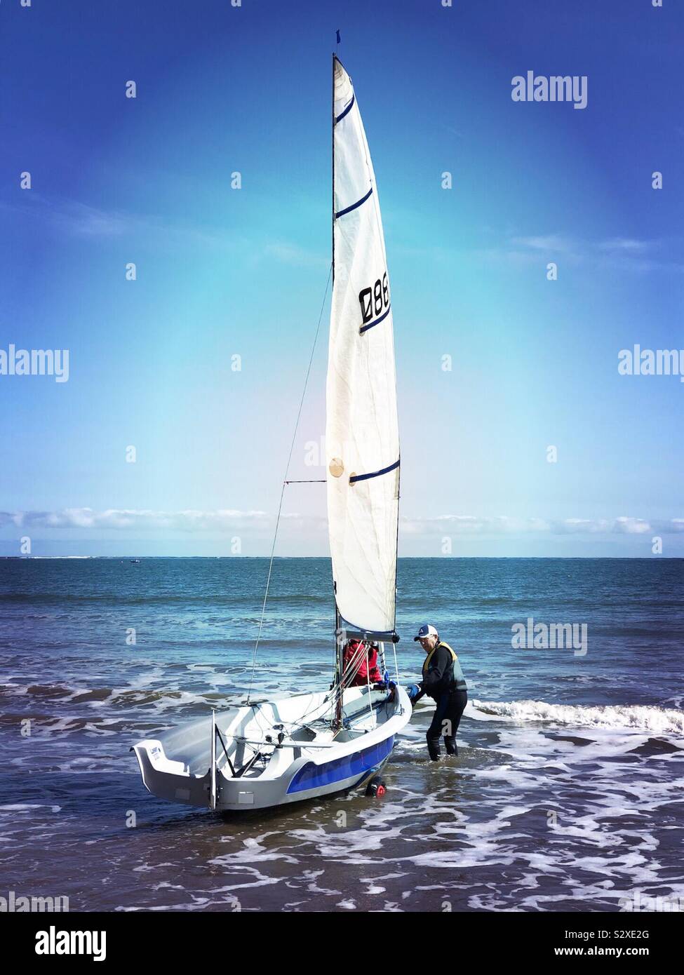 Two men launching a dinghy into the North Sea at Filey Bay Stock Photo