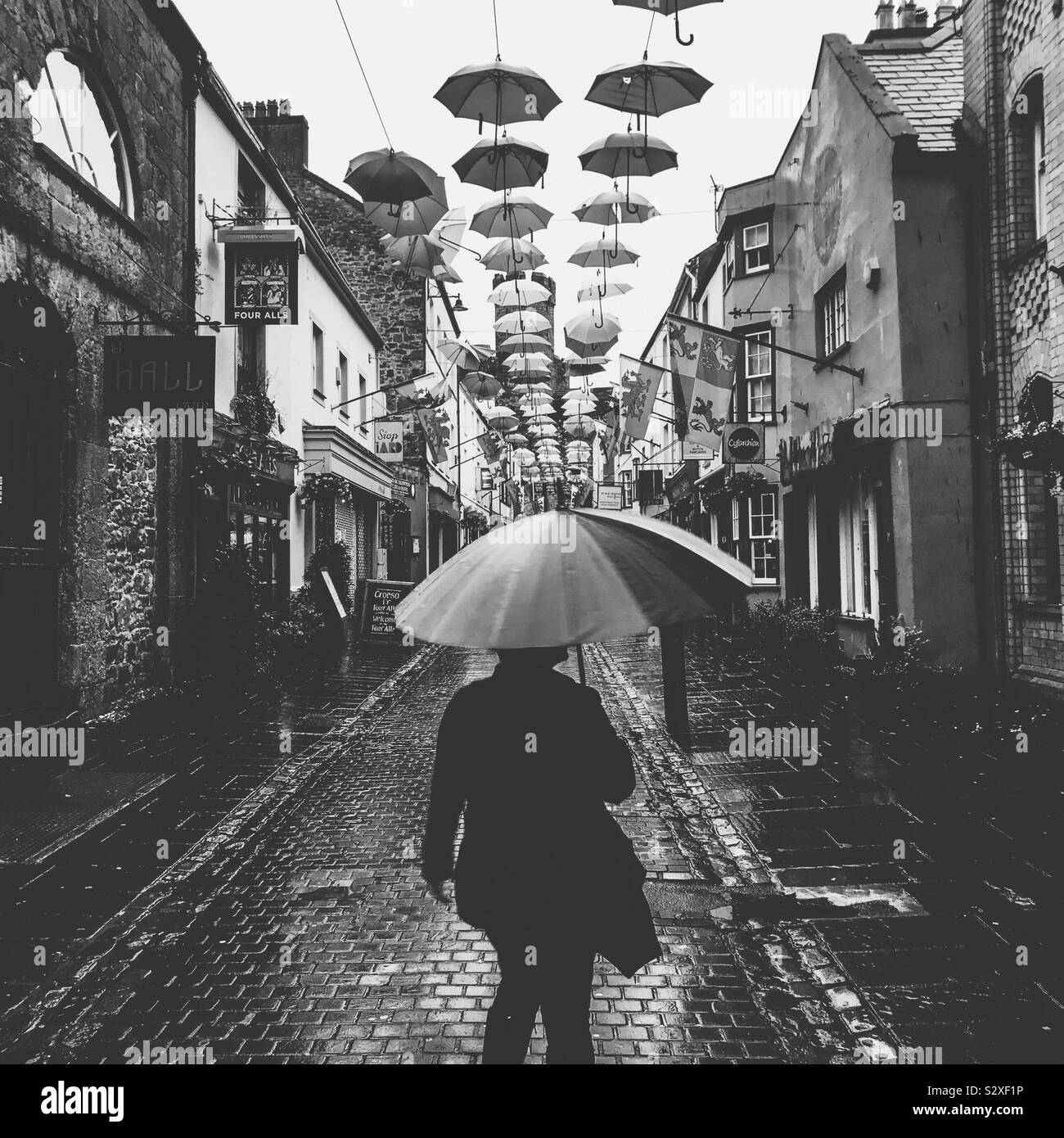 A rainy day down Palace Street in Caernarfon North Wales showing pedestrian carrying an umbrella underneath the 170 flying brollies art installation above Stock Photo
