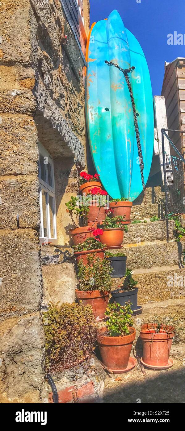 Stone Steps at The side Of A Cottage in Mousehole Cornwall UK with Plant Pots On Them and a Blue Surf Board At The Top - Smartphone Captured Stock Image Stone Steps at The side Of A Cottage in Mousehole Cornwall UK with Plant Pots On Them and a Blue Surf Board At The Top - Smartphone Captured Stock Image