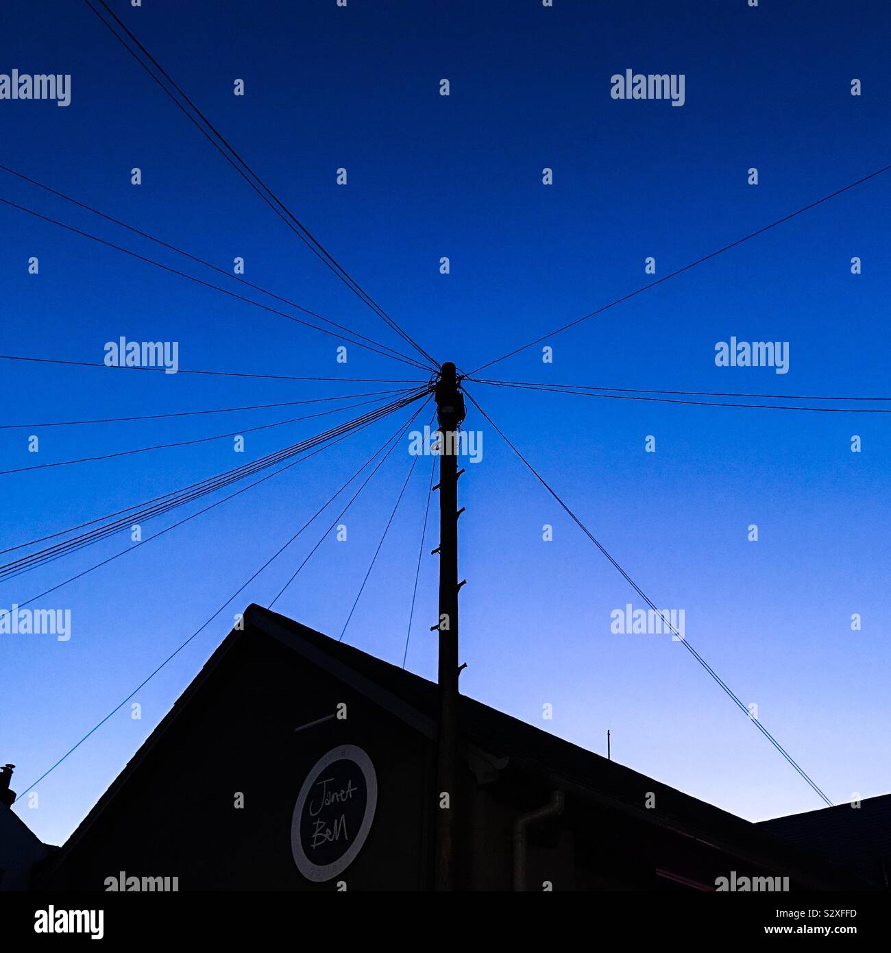 Warm glow of an evening sky in darkening blue above the roof tops and telegraph poles Stock Photo