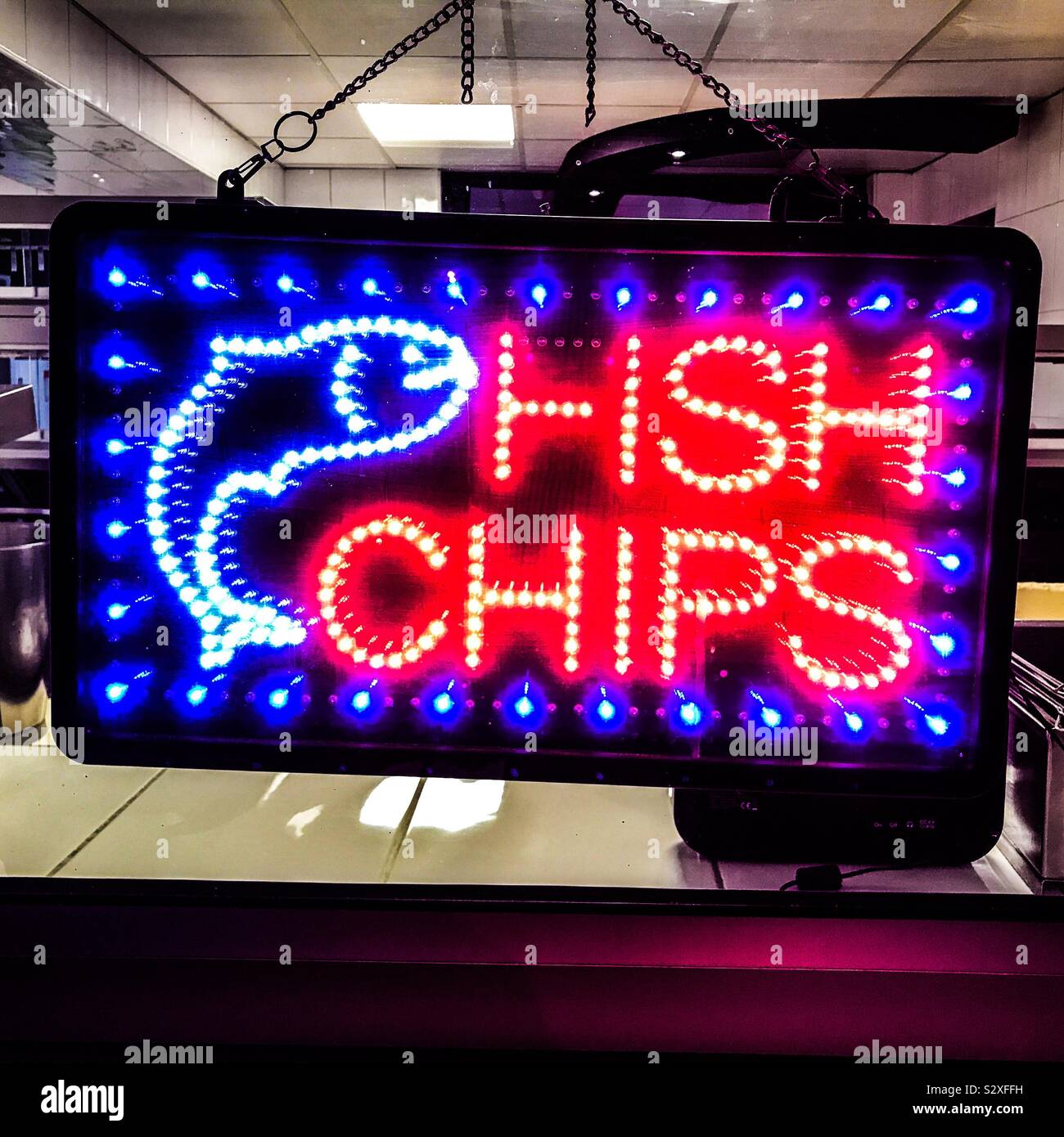 A bright orange white blue neon Fish and Chips sign signage in the back window looking in to a fish and chip shop premises Stock Photo