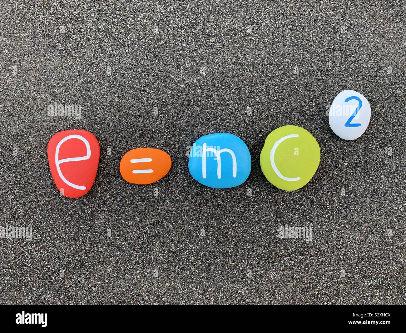 E=mc2 Theory of relativity composed with carved and colored stones over black volcanic sand - Smartphone Captured Stock Image