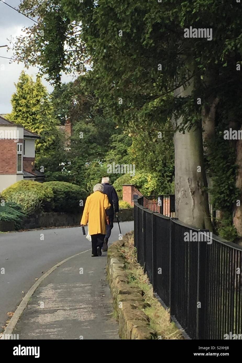 An elderly couple walk down a pathway alongside a suburban road. - Smartphone Captured Stock Image