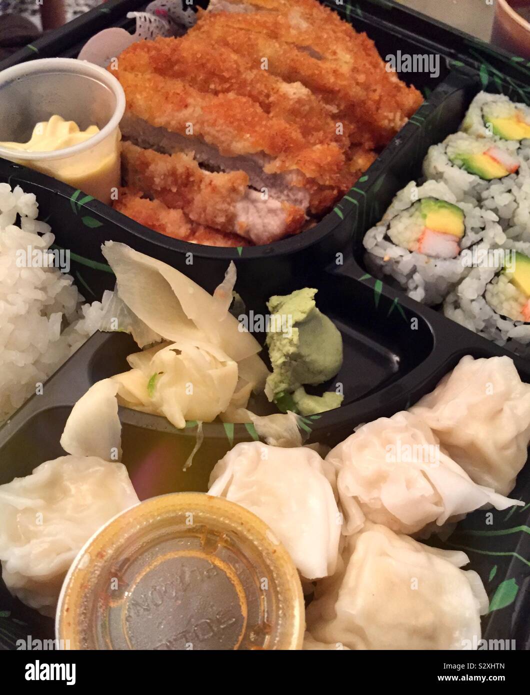 A Japanese restaurants bento box features dumplings,  California roll and Tonkatsu - Smartphone Captured Stock Image