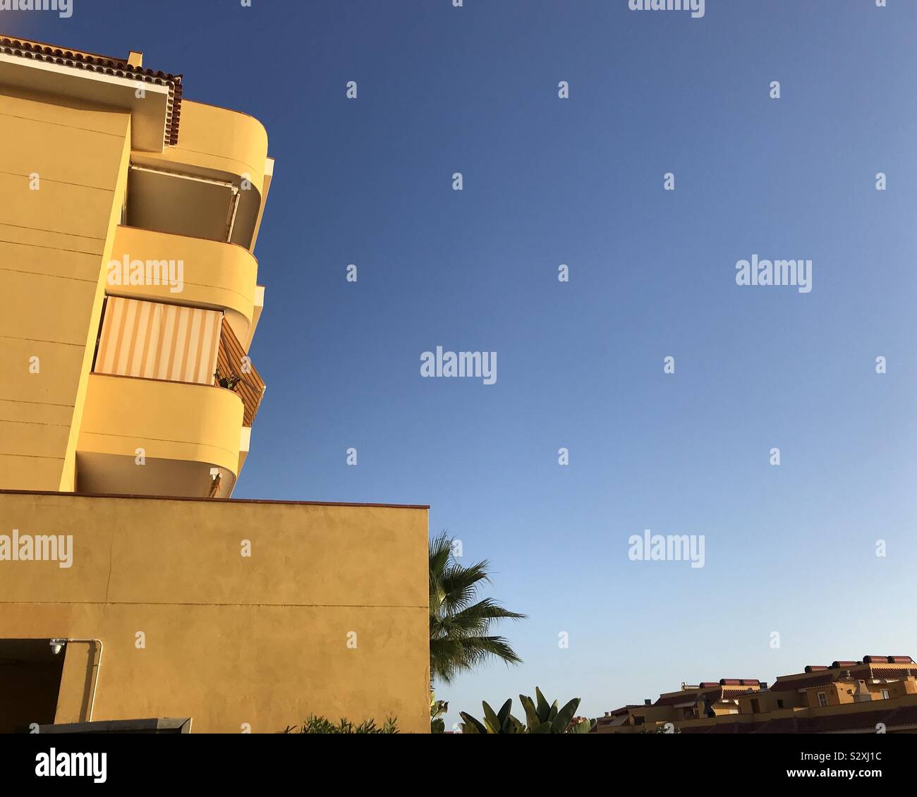 Mustard colored apartment block against a blue sky in Tenerife, Canary Islands - Smartphone Captured Stock Image