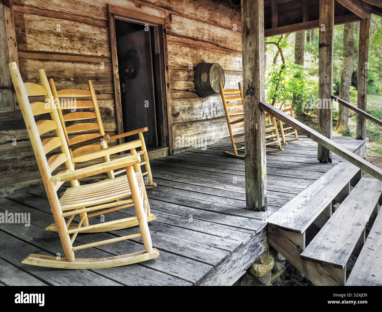 Empty wooden rocking chairs on the front porch of an old log house in the woods. This log house was built in the pioneer days of America during the 1830s. Stock Photo