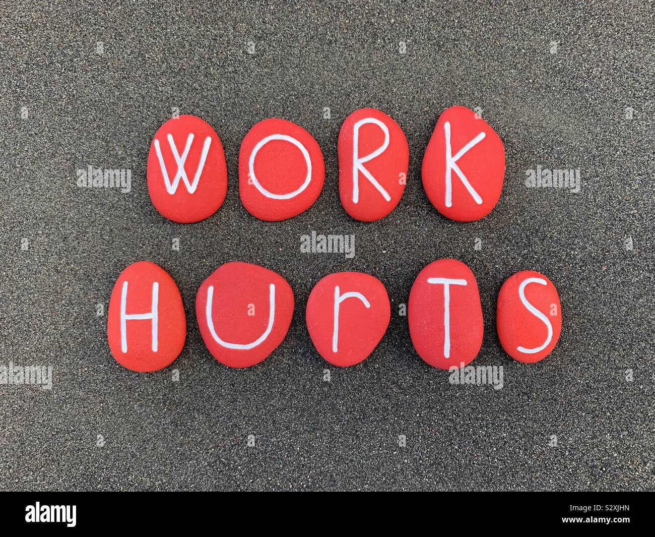 Work Hurts, ironic sentence composed with red colored and carved stones over black volcanic sand - Smartphone Captured Stock Image