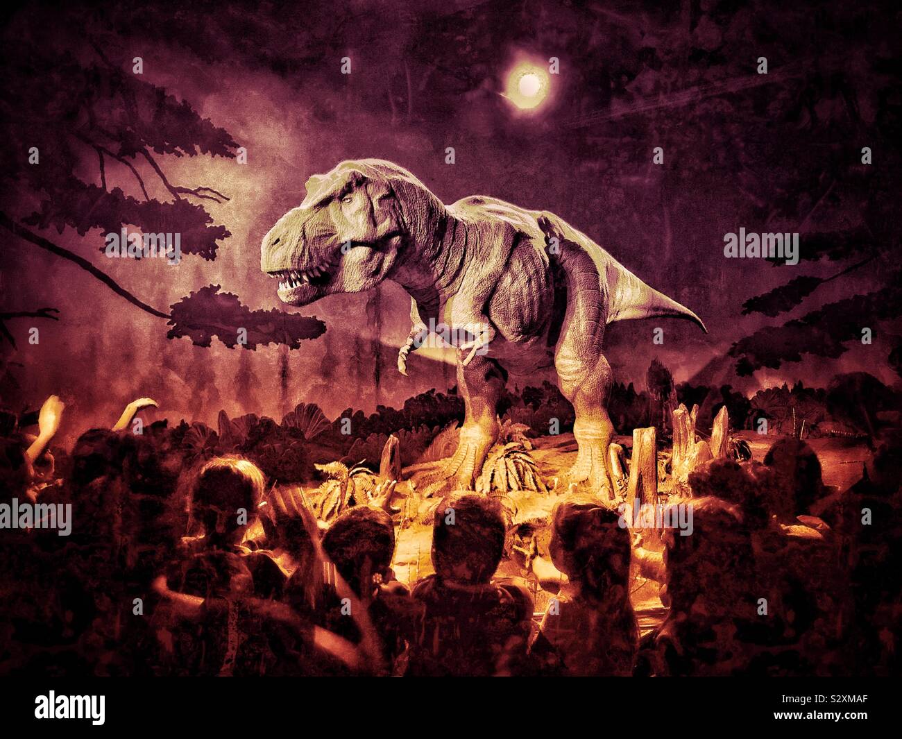 Children & adults surround and gaze in wonder at an exhibit of a lifelike T-REX Dinosaur at London’s Natural History Museum. The display has changing colours, with the model moving around & roaring. - Smartphone Captured Stock Image