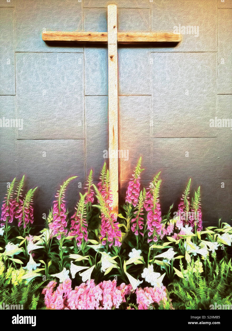 A Christian wooden cross hangs on a wall. It is surrounded by springtime Easter flowers such as foxglove and lilies. Stock Photo