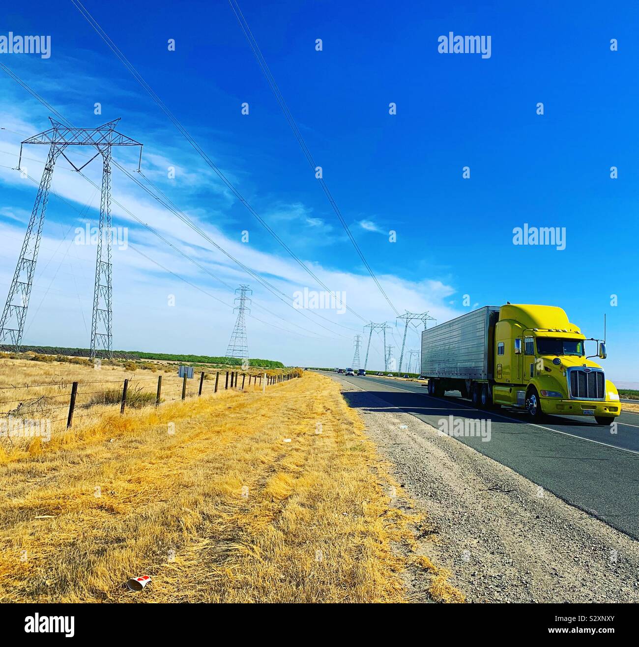 A truck with a yellow cab passes by transmission towers on a flat landscape under bright blue skies - Smartphone Captured Stock Image