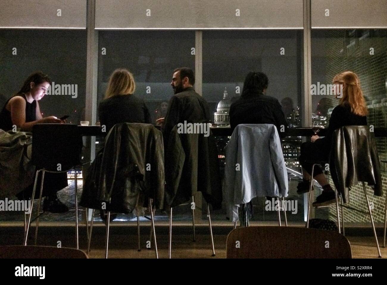A group of chic people in a bar with windows overlooking St Paul’s Cathedral at night time - Smartphone Captured Stock Image