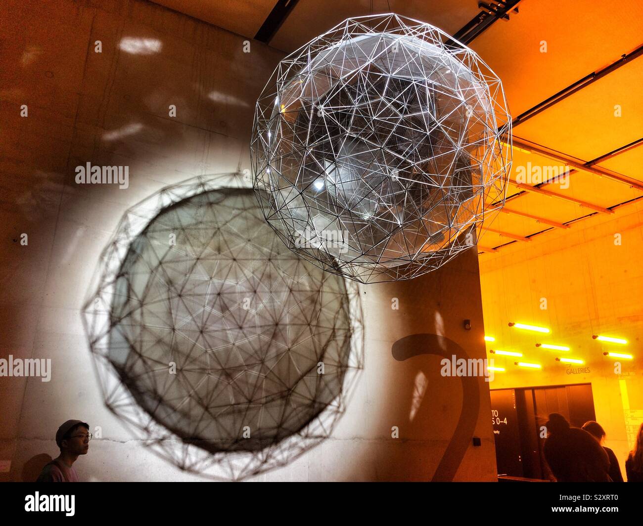A man viewing a sculpture suspended from the ceiling of an art gallery - Smartphone Captured Stock Image