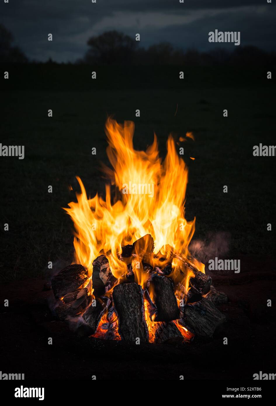 A roaring camp fire or bonfire with flickering orange flames at night in close up with copy space - Smartphone Captured Stock Image