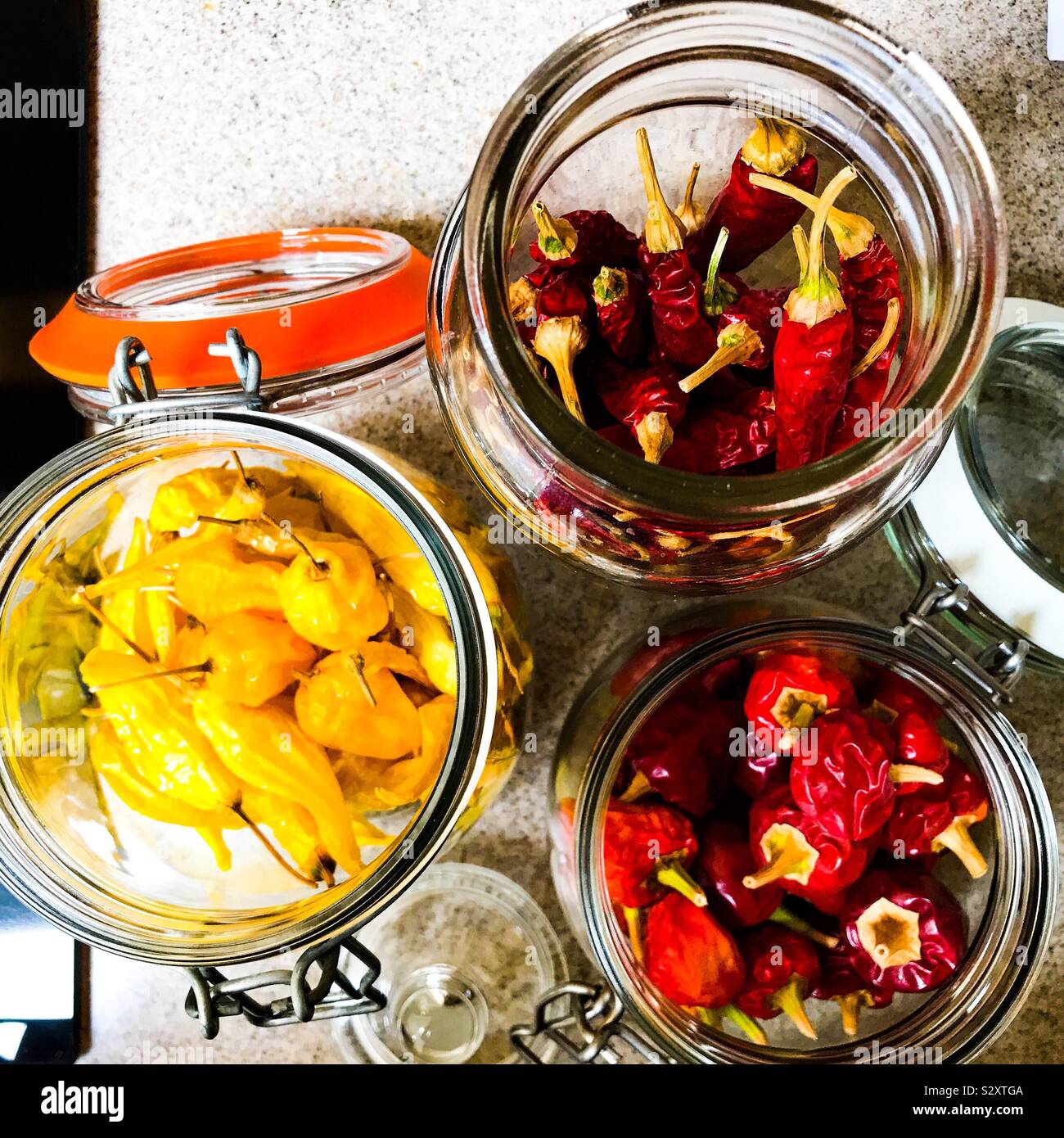 Red and yellow chillis in open Kilner jars on Corian kitchen work surface Stock Photo