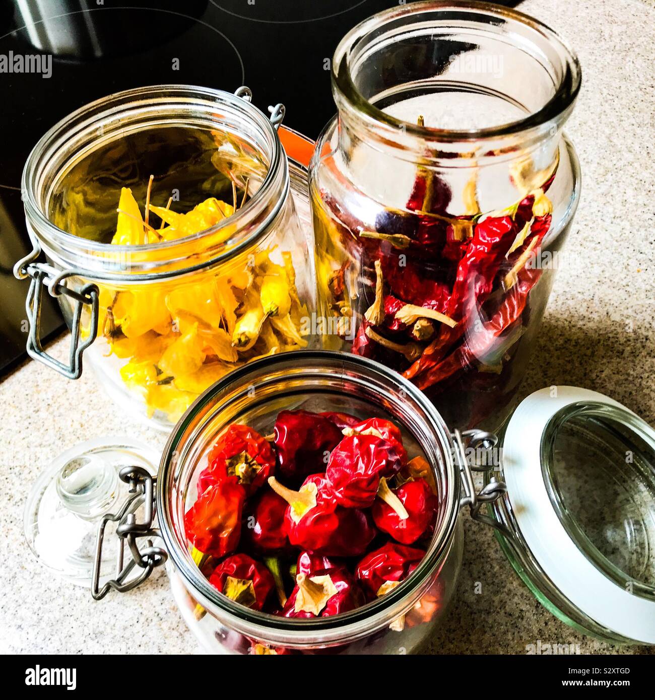 Red and yellow dried chillis in open Kilner jar storage on Corian kitchen work surface Stock Photo