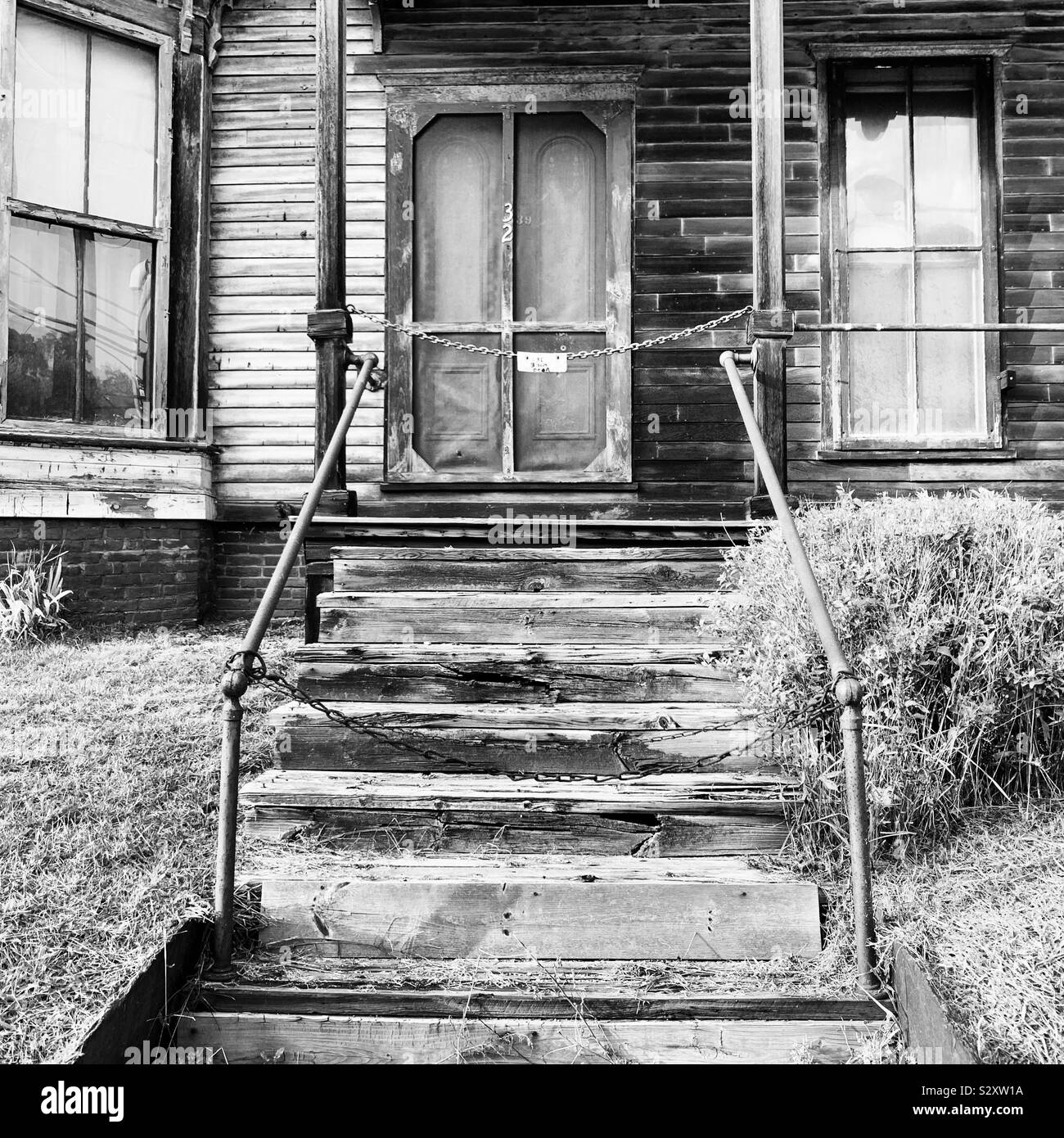 Black and white image of blocked-off stairs in front of the entrance to an old home - Smartphone Captured Stock Image