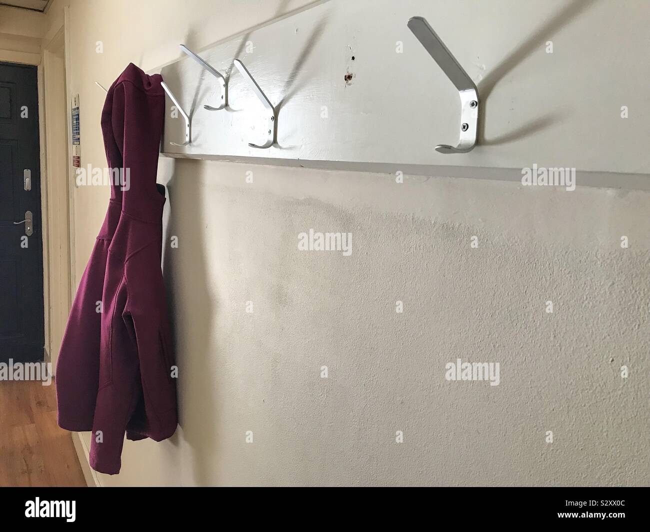 A single hooded top hangs alone on coat hooks in a corridor. - Smartphone Captured Stock Image