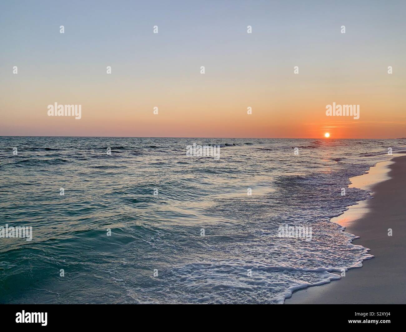 Colorful sunset on the beach with view of sun on the horizon and ocean waves - Smartphone Captured Stock Image