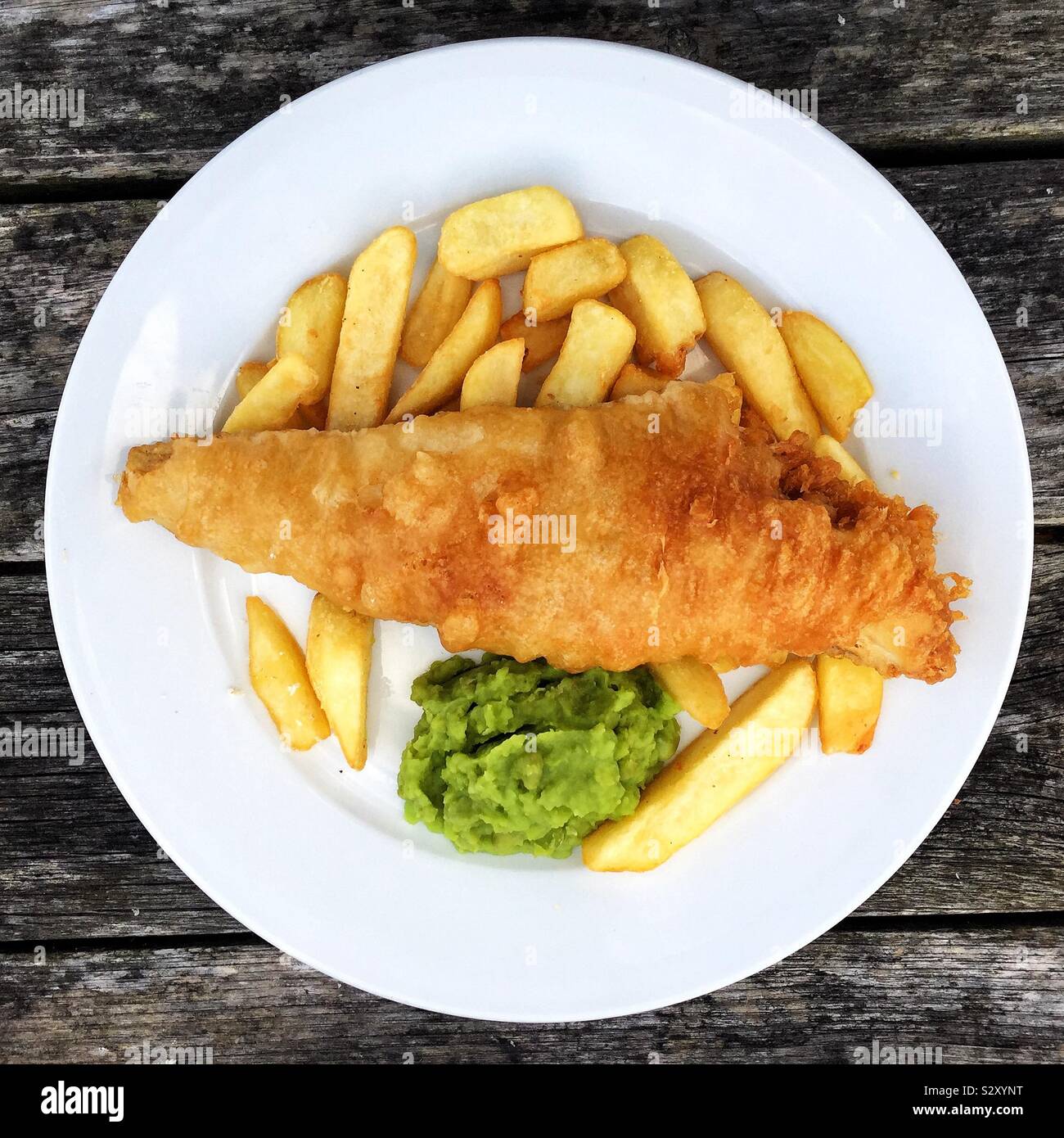 Looking down from above onto a plate full of fish and chips with mushy peas and copy space Stock Photo