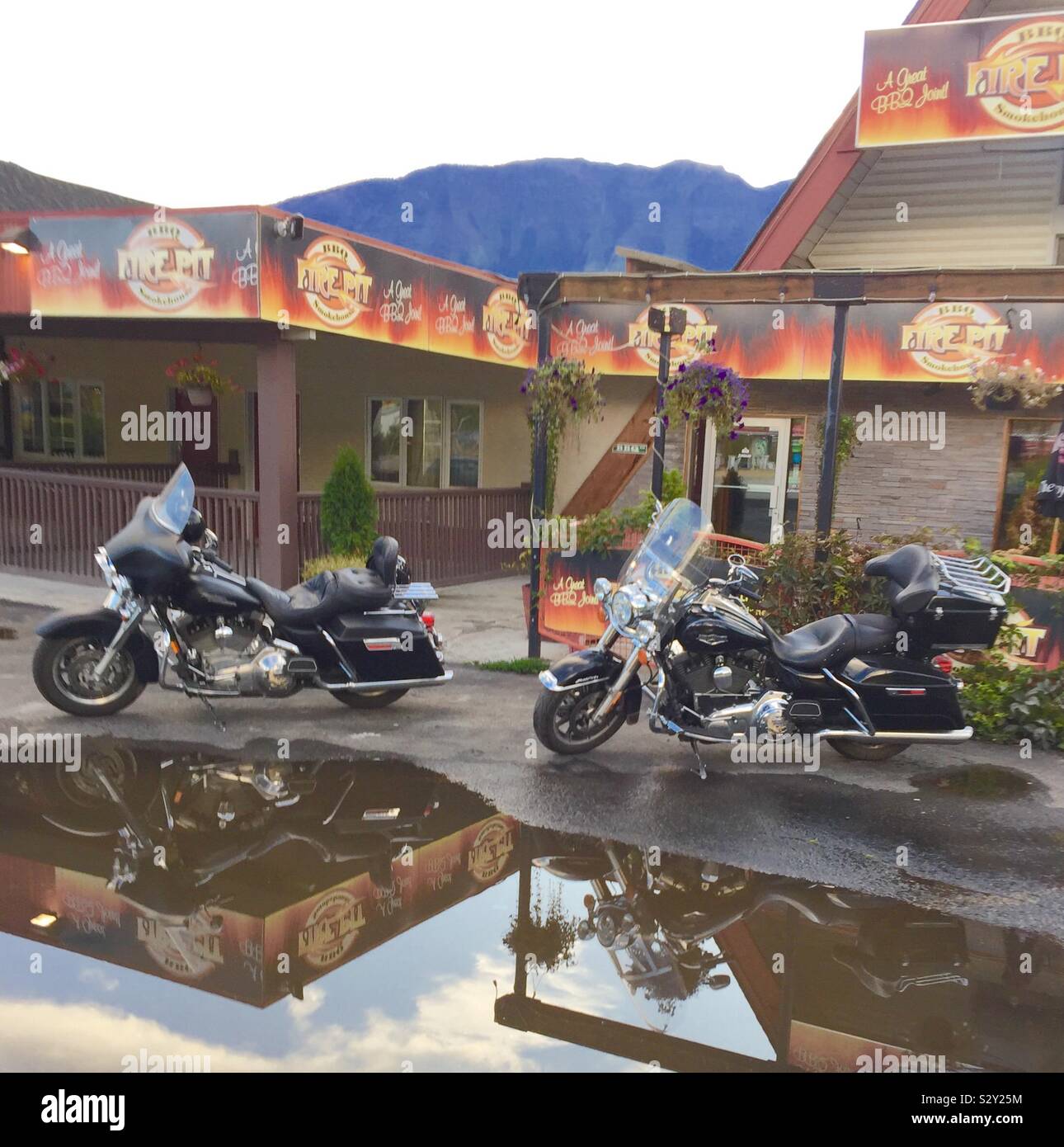 Two parked motor cycles reflected in a puddle in Golden, BC, Canada - Smartphone Captured Stock Image