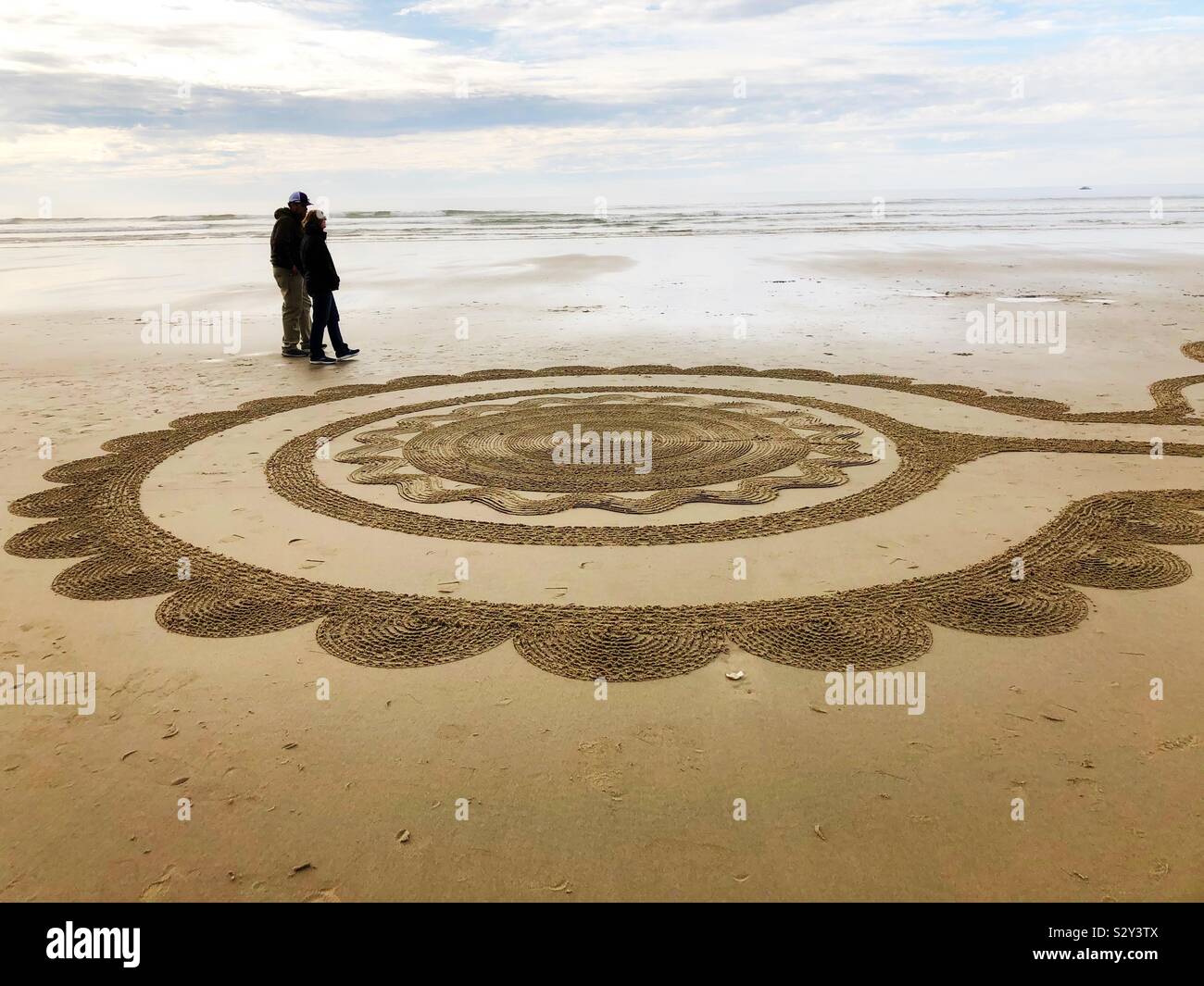 A couple walking next to a section of a sand labyrinth in Florence, Oregon. Stock Photo