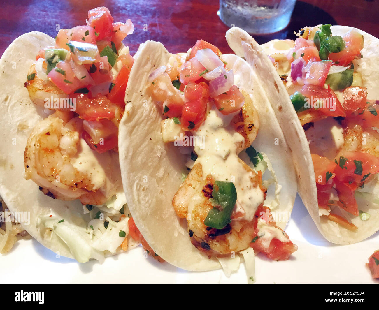 A serving of three grilled shrimp tacos smothered with fresh pico de gallo and spicy chipotle sauce. Stock Photo