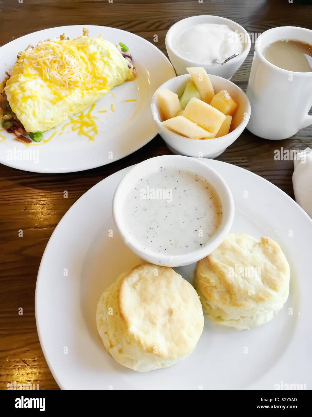 Homemade buttermilk biscuits served with gravy. There’s also an egg omelet and a bowl of fresh fruit. Coffee is the drink of choice. Stock Photo