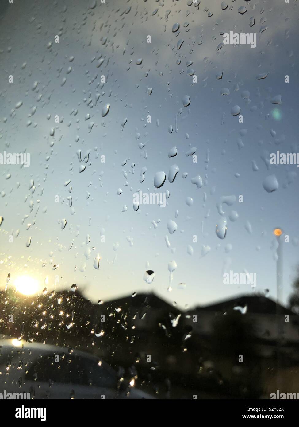 Close up of rain on a window at sunset  overlooking a car park, street light and houses - Smartphone Captured Stock Image