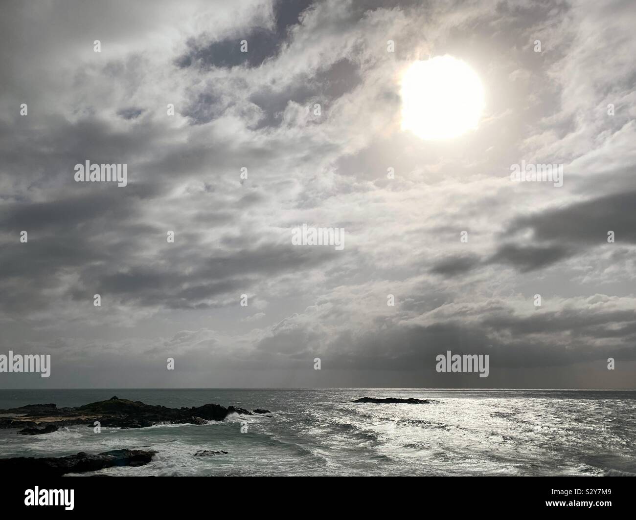 Windy day with the sun like a huge glowing globe behind the clouds as the barely there waves ripple in to the beach - Smartphone Captured Stock Image