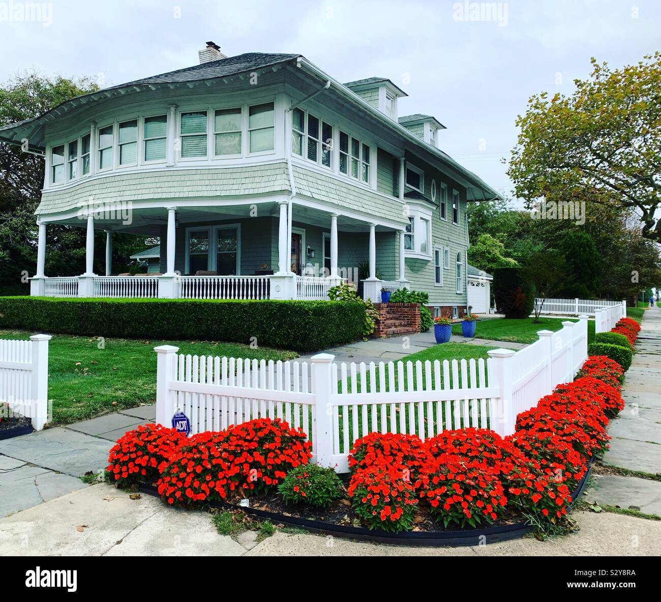 Orange flowers and a white fence in front of a home in Allenhurst, Monmouth County, New Jersey, United States - Smartphone Captured Stock Image