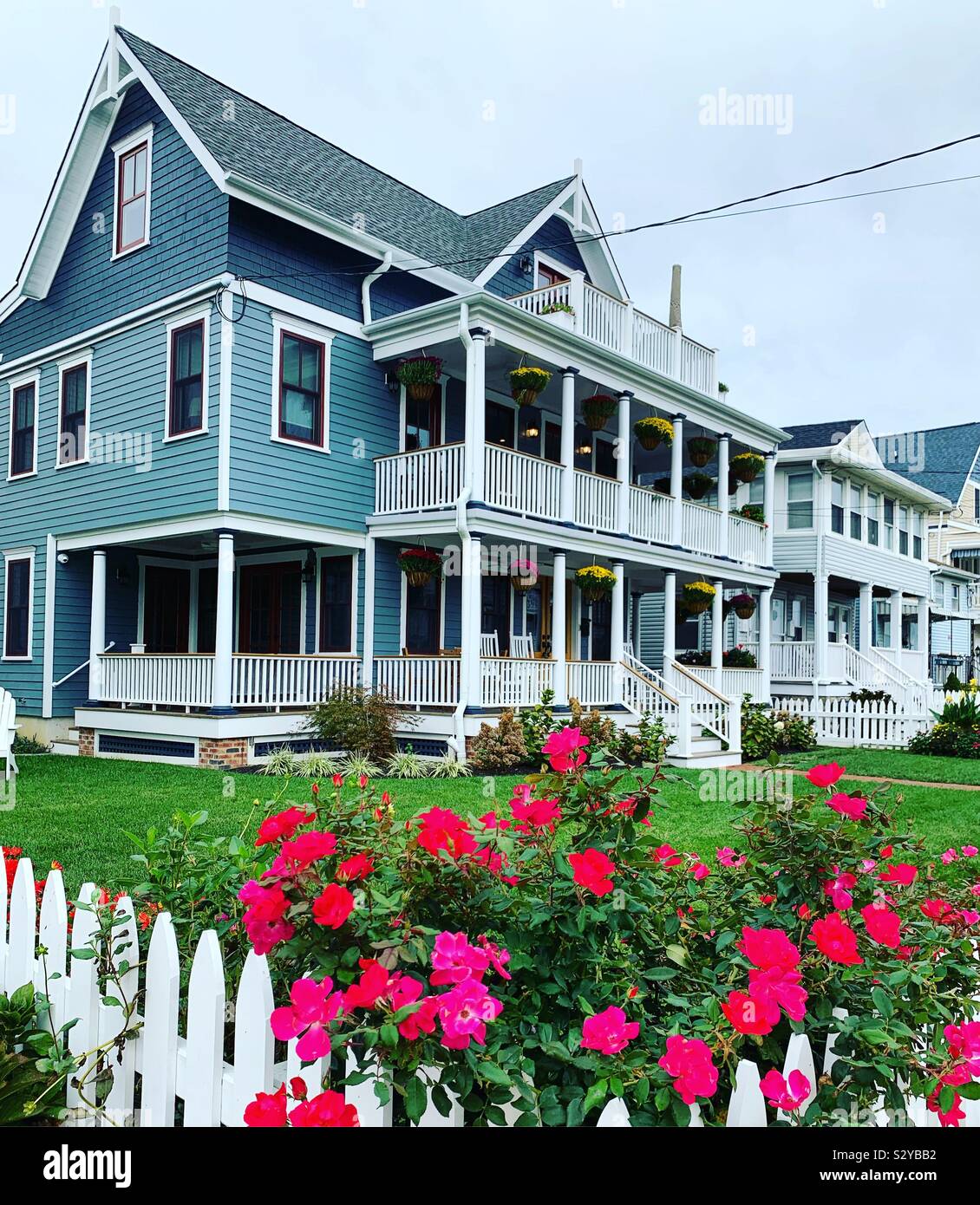 Flowers around a white picket fence, Victorian architecture in the background, Ocean Grove, Neptune Township, Monmouth County, New Jersey, United States - Smartphone Captured Stock Image