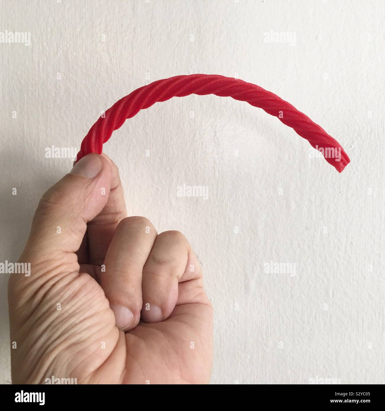 Caucasian hand holding a piece of red licorice against a white background - Smartphone Captured Stock Image