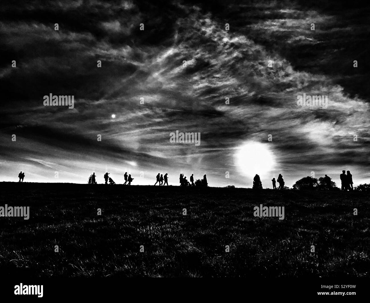 Dramatic monochrome image of silhouette’s of people on a hill photographed from far distance during sunset in London UK Stock Photo