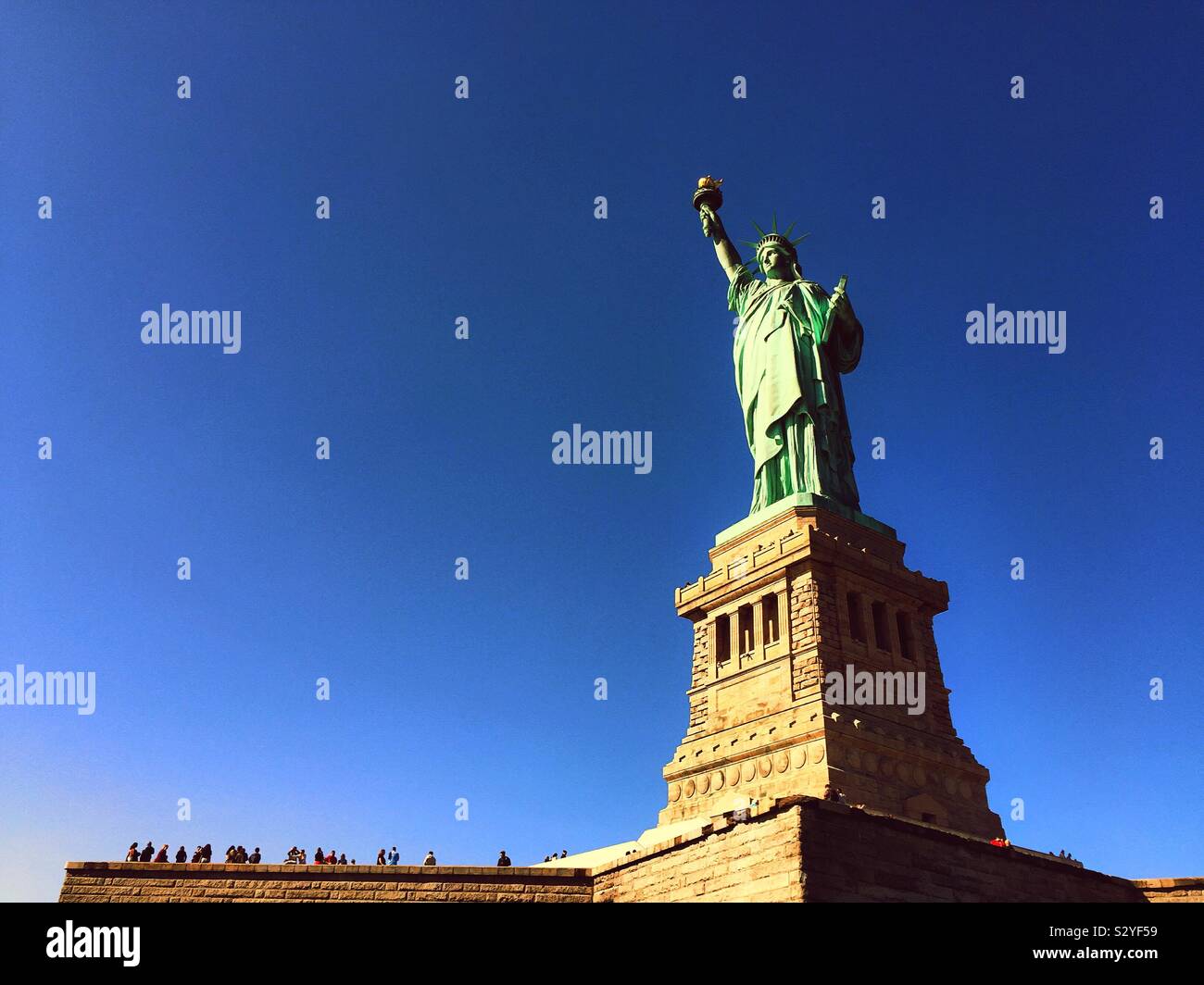 Tourists flock to the pedestal of the Statue of Liberty on liberty Island in New York Harbor on a clear blue cloudless day, NYC, USA - Smartphone Captured Stock Image