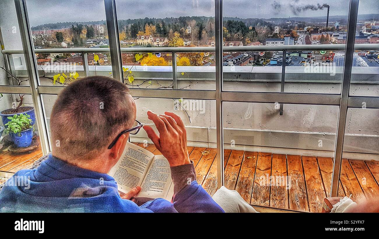 Man reading book on high rise enclosed terrace with panoramic view, Sweden Stock Photo