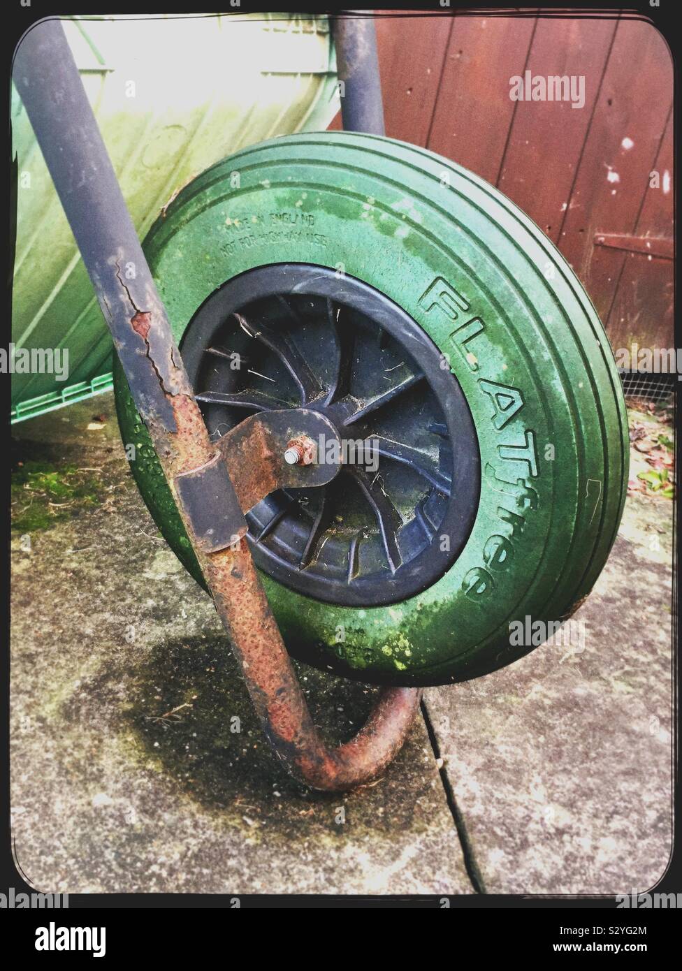 Green wheel of an upturned wheelbarrow on a garden lawn Stock Photo